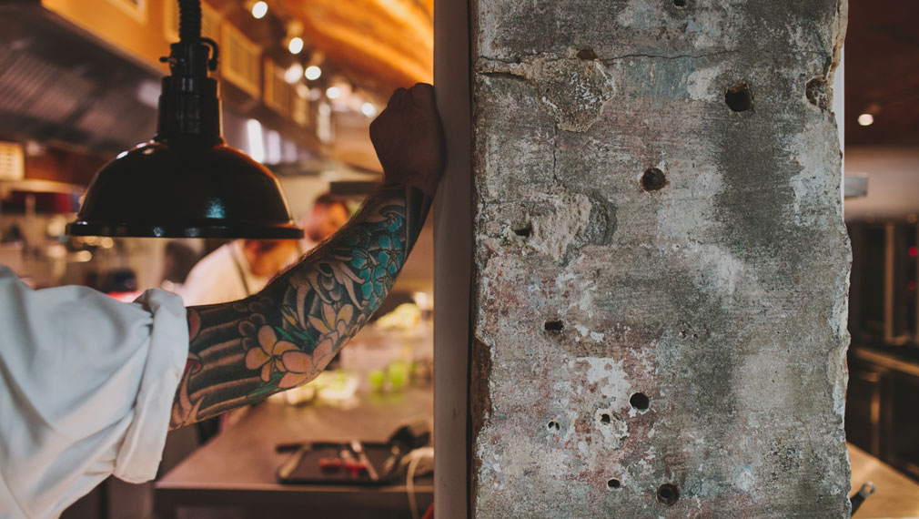 Alex Bond's tattood arm leaning on concrete pillar