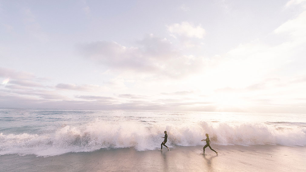 A couple run into the waves as the sun rises