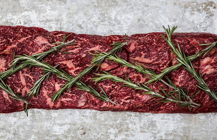 Still life photography of locally sourced and foraged sirloin of beef with rosemary on a baking tray